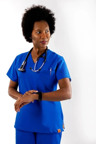 Confident female healthcare professional wearing royal blue Estiva scrubs top with stethoscope and smartwatch.