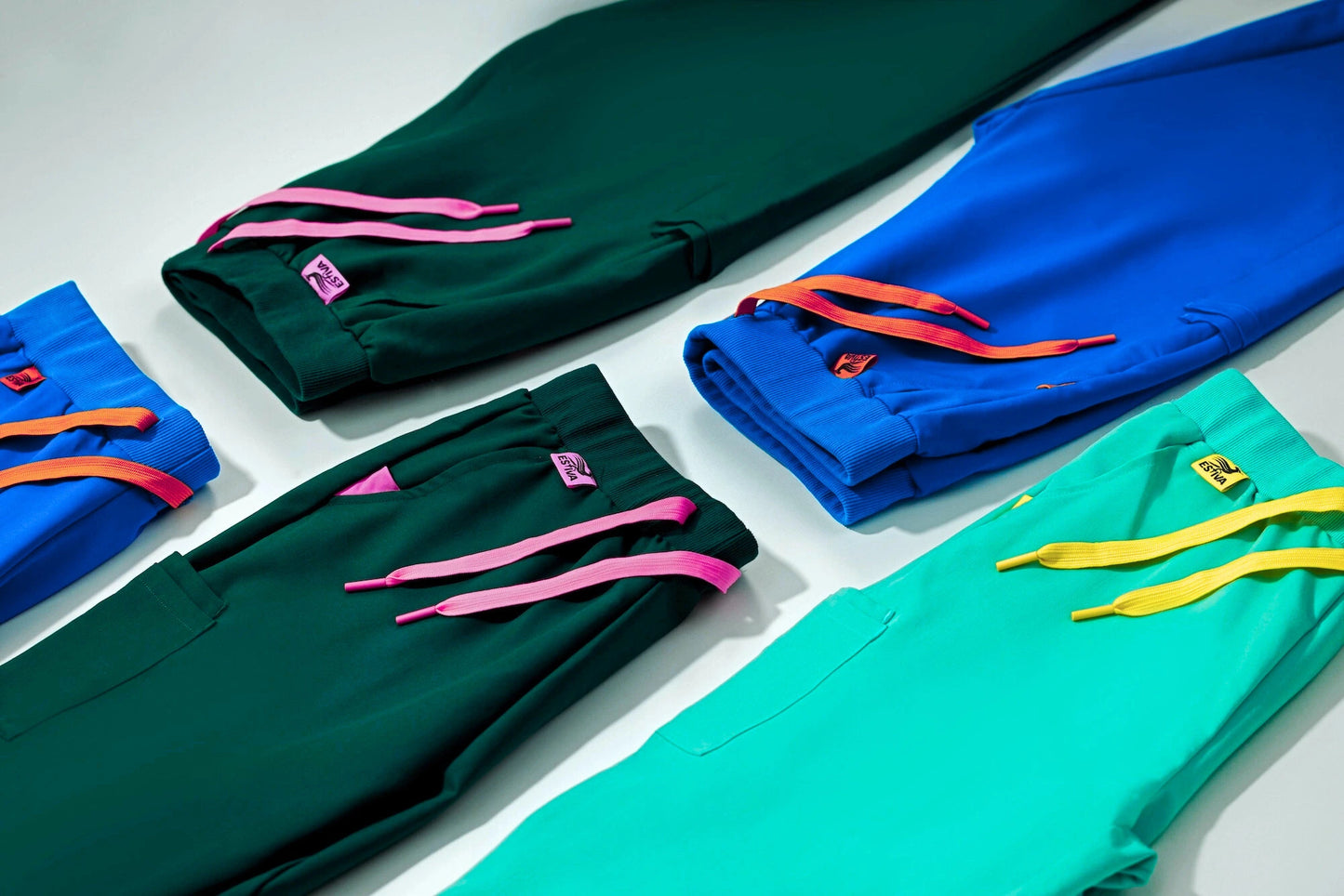 Colorful Estiva scrub pants with signature drawstring details in teal, royal blue, deep green, and turquoise, designed for comfort and style.