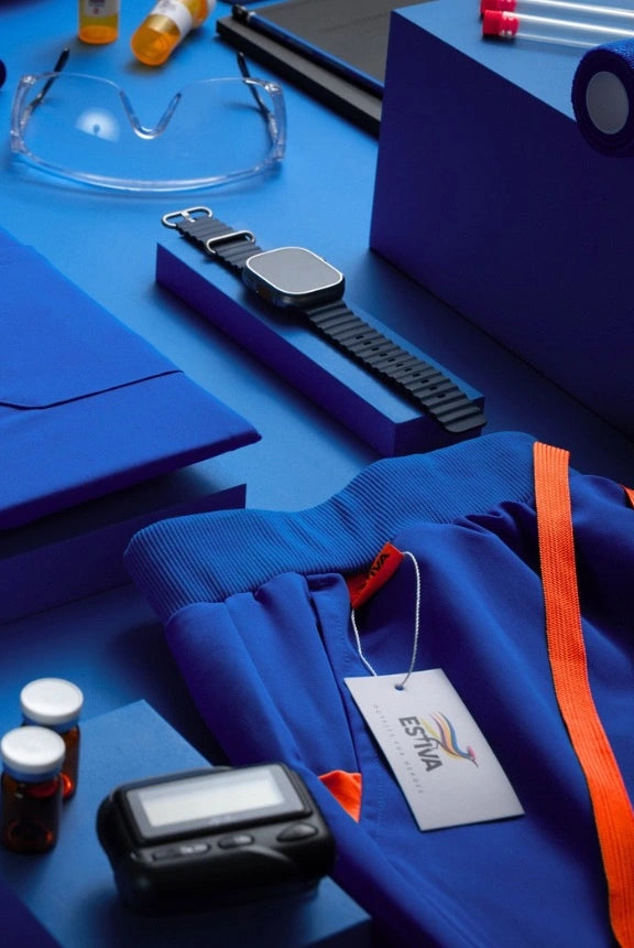 Royal blue Estiva scrubs with orange drawstring, smartwatch, pager, and medical essentials on a flat lay background