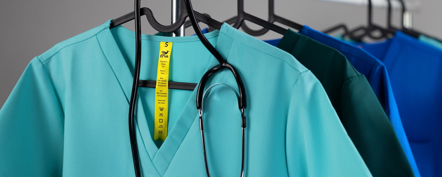 Women’s medical scrubs by Estiva hanging on rack, premium scrub tops in turquoise, deep teal and royal blue, made in USA
